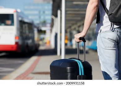 Passenger waiting at bus station in front of airport terminal. Selective focus on hand holding suitcace. - Powered by Shutterstock