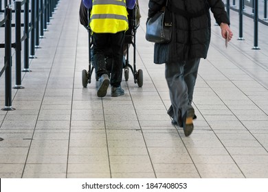 Passenger Walking To Airport Departure Gate, Assistance Staff Helping With Person On Wheel Chair, View From Behind