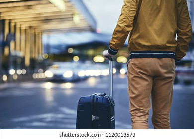 Passenger walking outside airport terminal. Rear view of young man with luggage at night. - Powered by Shutterstock