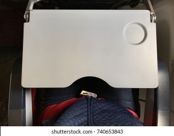 Passenger Who Wears Blue Jeans Is Fastening  Red Seat Belt In Airplane Cabin. There Are Tray Table And Seat Belt For Passenger In Each Chair On The Plane.