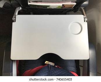 Passenger Who Wears Blue Jeans Is Fastening  Red Seat Belt In Airplane Cabin. There Are Tray Table And Seat Belt For Passenger In Each Chair On The Plane.