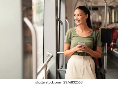 Passenger woman browsing on phone in tram indoor, standing enjoying her journey through the city inside a modern streetcar, looking aside while texting. Commute and connectivity - Powered by Shutterstock