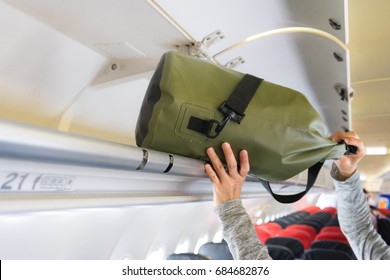 Passenger woman putting luggage into overhead locker on airplane (Selective focus)