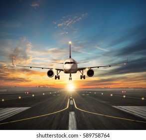 Passengers airplane landing to airport runway in beautiful sunset light, silhouette of modern city on background