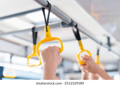 Passengers holding yellow hand grips on a public transport vehicle during a morning commute - Powered by Shutterstock