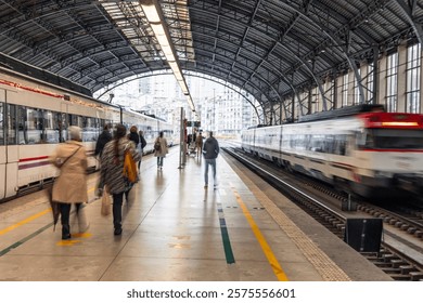 Passengers walking on the platform of a train station with a high-speed train departing in Bilbao, Spain, creating a sense of motion and travel