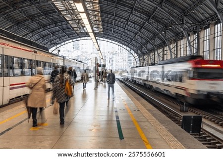 Passengers walking on the platform of a train station with a high-speed train departing in Bilbao, Spain, creating a sense of motion and travel