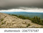 Passing dark rain cloud floating by, seen from the exposed granite summit of Mt. Kearsarge, at Winslow State Park in Wilmot, New Hampshire