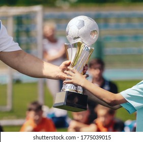 Passing of the Soccer Trophy Moment. Young Player Awarding Trophy Closeup. Child as a Team Captain Winning Sport Football Championship. Adult Person Passing Trophy to Kid Player - Powered by Shutterstock