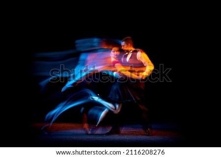 Passion. Dynamic portrait of young ballroom dancers dancing Argentine tango isolated on dark background with neon mixed light. Concept of art, beauty, grace, action, emotions. Copy space for ad
