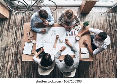 Passionate About Their Project. Top View Of Young Modern People In Smart Casual Wear Working With Blueprint While Sitting In The Creative Office