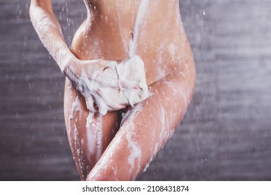 Passionate beautiful young naked woman taking shower, washing herself with a wisp of bast and covering her intimate zone, close-up