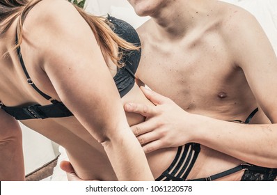passionate couple in an erotic situation stroking each other. woman in black lingerie garter belt and bra. he holds his hands at her waist. without faces.