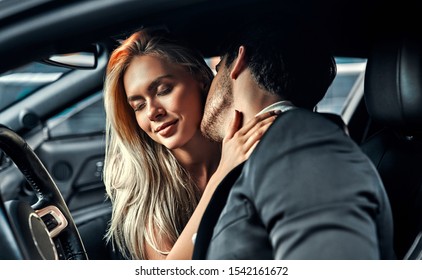 Passionate couple making love in car. Attractive blonde in elegant black dress and handsome businessman in suit are kissing in car.