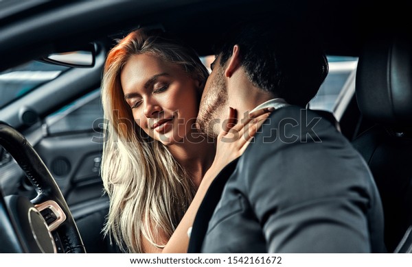 Passionate couple making love in car. Attractive\
blonde in elegant black dress and handsome businessman in suit are\
kissing in car.
