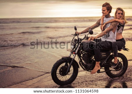 passionate couple riding motorcycle on ocean beach during sunrise