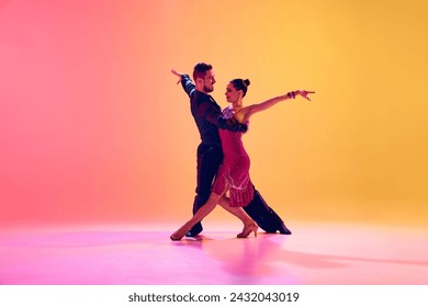 Passionate dancers. Artistic, talented young man and woman in motion in beautiful stage costumes dancing ballroom against gradient pink yellow background in neon light. Concept of dance class, art - Powered by Shutterstock