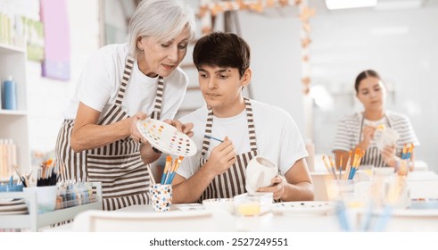 Passionate elderly female teacher offering guidance to interested young guy painting ceramic mug in pottery class. Creative hobby concept.. - Powered by Shutterstock