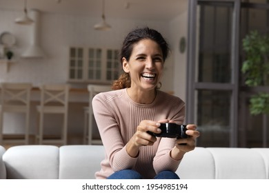 Passionate Gamer. Excited Millennial Hispanic Woman Spend Leisure Time For Playing Console Videogame. Overjoyed Young Latina Female Sit On Cozy Sofa At Home Hold Gamepad Enjoy Favorite Computer Game