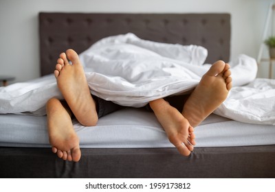Passionate interracial couple making love in bed at home, closeup of feet. Unrecognizable young lovers engaged in intimate foreplay, having sex, receiving erotic pleasure