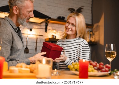 Passionate middle-aged couple sharing present on a romantic date in the kitchen. Love language - gift receiving. Celebration of anniversary Valentine`s day Christmas special event - Powered by Shutterstock