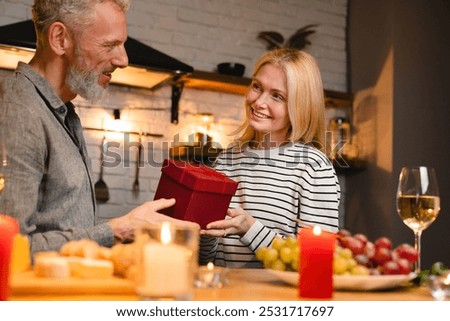 Passionate middle-aged couple sharing present on a romantic date in the kitchen. Love language - gift receiving. Celebration of anniversary Valentine`s day Christmas special event