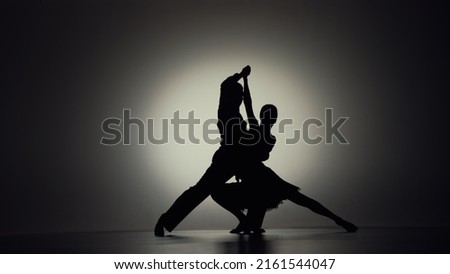 Passionate tango choreography elements performed by pair of ballroom dancers. Black silhouettes of man and woman moving on gray background with backlight. Slow motion ready, 4K at 59.94fps.