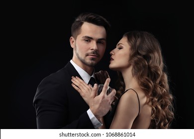 Passionate woman and handsome man using perfume on black background