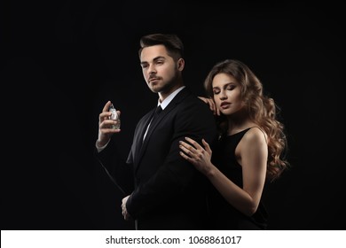 Passionate woman and handsome man using perfume on black background