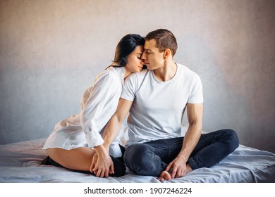 A passionate woman hugging a man tenderly and kissing him romantically. Young gentle lover, sitting on the bed, enjoying the touch of sensual sexy lady, moaning with desire during sex.