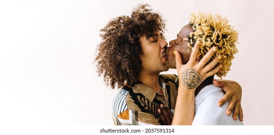 Passionate Young Gay Couple Kissing Each Other. Two Young Male Lovers Sharing An Affectionate Moment While Embracing Each Other. Young Gay Couple Standing Together Against A Studio Background.