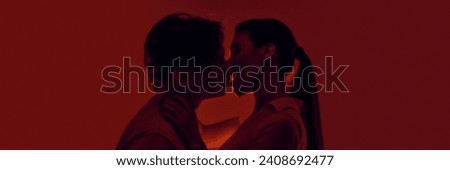 Passionate young man and woman, young couple kissing, expressing love against red background in neon light. Monochrome. Concept of romance, love, relationship, passion, youth. Banner