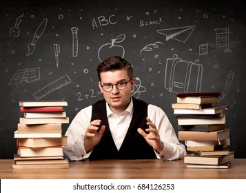 Ein leidenschaftlicher junger Lehrer, der an einem Schreibtisch sitzt, mit einem Stapel Bücher vor der Tafel, die voll von zurück zu den Schulartikeln Konzept gezogen.