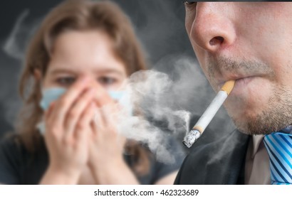 Passive smoking concept. Man is smoking cigarette and woman is covering her face. A lot of smoke around.