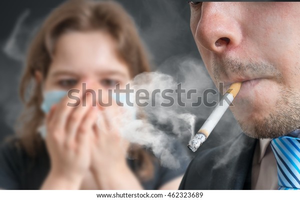 Passive smoking concept. Man\
is smoking cigarette and woman is covering her face. A lot of smoke\
around.