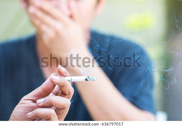 Passive smoking concept. Man is\
smoking cigarette and man is covering face. A lot of smoke\
around.