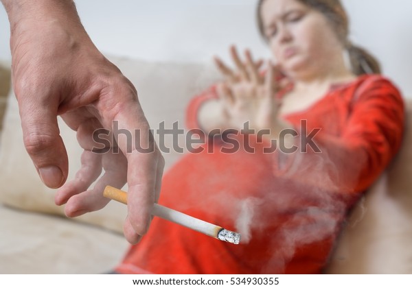 Passive smoking in pregnancy.\
Selfish man is smoking cigarette. Pregnant woman in\
background.