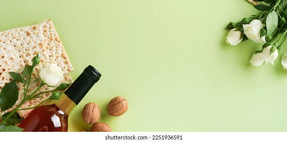 Passover celebration concept. Matzah, red kosher wine, walnut and spring beautiful rose flowers. Traditional ritual Jewish bread on light green background. Passover food. Pesach Jewish holiday. Banner