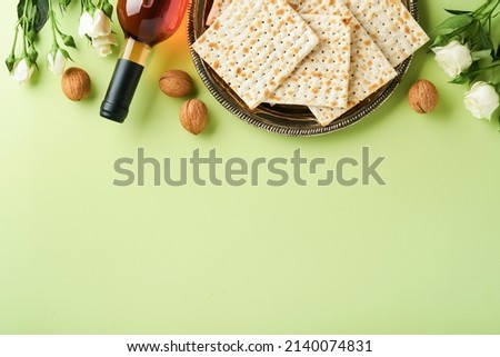 Passover celebration concept. Matzah, red kosher wine, walnut and spring beautiful rose flowers. Traditional ritual Jewish bread on light green background. Passover food. Pesach Jewish holiday.