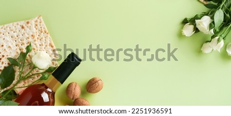 Passover celebration concept. Matzah, red kosher wine, walnut and spring beautiful rose flowers. Traditional ritual Jewish bread on light green background. Passover food. Pesach Jewish holiday. Banner