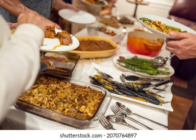 Passover Seder Potluck With Family Gathered Aroudn The Food, Serving Themselves Dinner.  Traditional Passover Meal With Brisket.