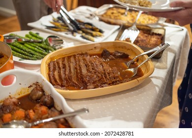 Passover Seder Potluck With Family Gathered Aroudn The Food, Serving Themselves Dinner.  Traditional Passover Meal With Brisket.