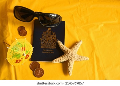 Passport, starfish, foreign coins dark sunglasses and tiny umbrella on bright yellow background with copy space for tourism 