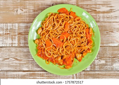Pasta with carrots and meat in a green plate on a wooden table. Vermicelli with orange sauce on a pink shabby board. Place for text near the plate. Copy space for design.
