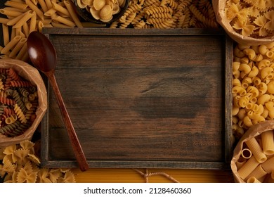 pasta concept some of the types of pasta in the container and some put on the ground being arranged surrounding a wooden board with a wooden spoon. - Powered by Shutterstock