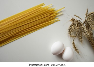 Pasta And Eggs. Pasta From Durum Wheat, Close-up. Egg With Yolk And Ears Of Wheat On White Background. Pasta And Grains Of Wheat. Ingredients For Cooking Pasta. Сopy Space, Overhead View, Layout