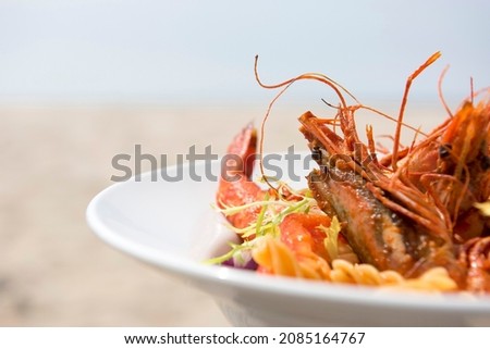 Pasta with fresh lobster in a white deep plate. Tasty and colorful. Pasta, lobster, lettuce and tomato. On a robust table in a restaurant. Sunlight. The sea in the background.