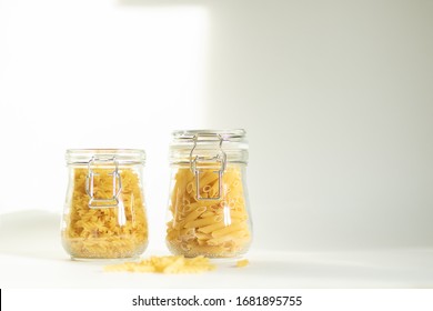 Pasta In A Glass Jar On A White Background. Two Containers Stand On A Table In Daylight, A Shadow Falls From The Dishes. Safe Food Storage For Future Use.