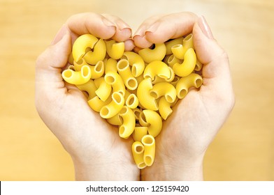 Pasta gomito in woman's  hands forming heart shape