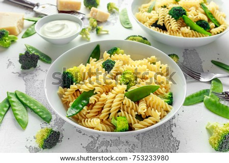 Pasta with green vegetables broccoli, Mange tout and creamy sauce in white plate.